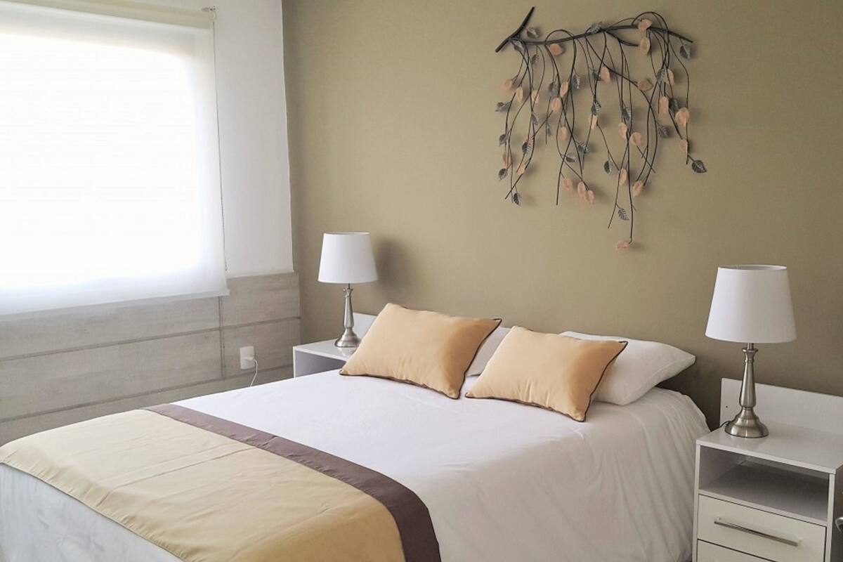 A neatly made bed with two pillows, a bedside table with a lamp, and a wall decoration.