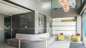 Eine moderne Lobby mit einem grauen Sofa, Holztischen und grünen Stühlen.