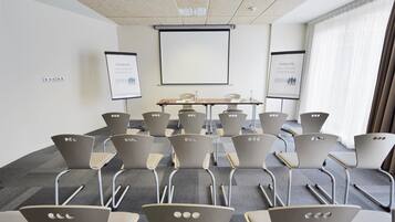 Uma sala de conferências com tela de projetor, quadro branco e mesa com cadeiras.