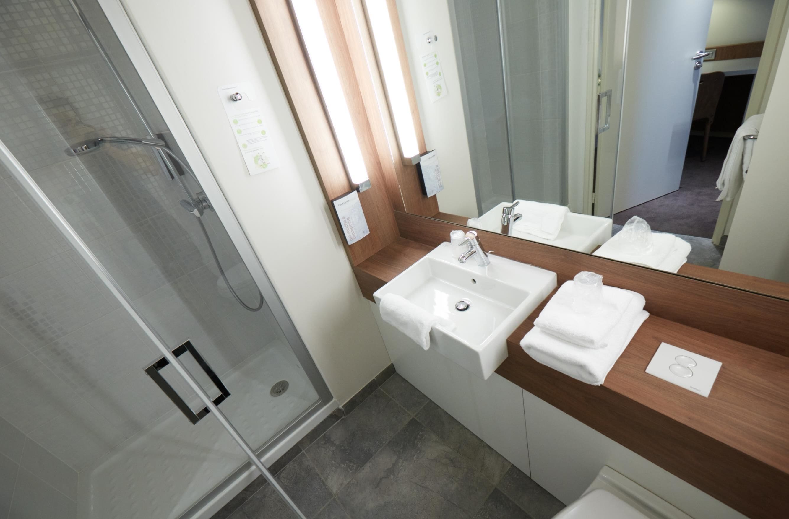 A modern bathroom with a glass shower enclosure, a wooden vanity with a mirror, and a white sink.