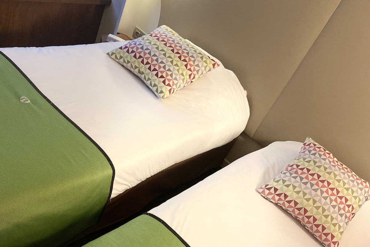 Two twin beds with green bedspreads and patterned pillows in a hotel room.