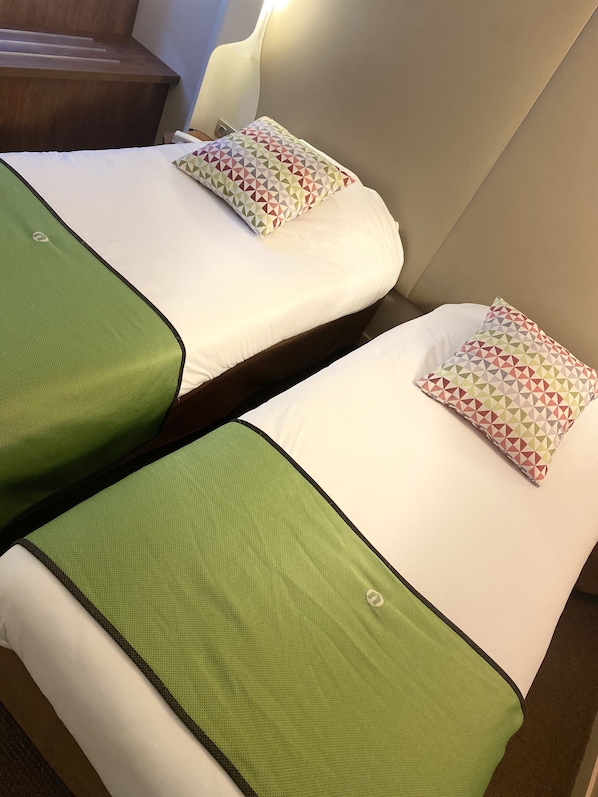 Two twin beds with green bedspreads and patterned pillows in a hotel room.