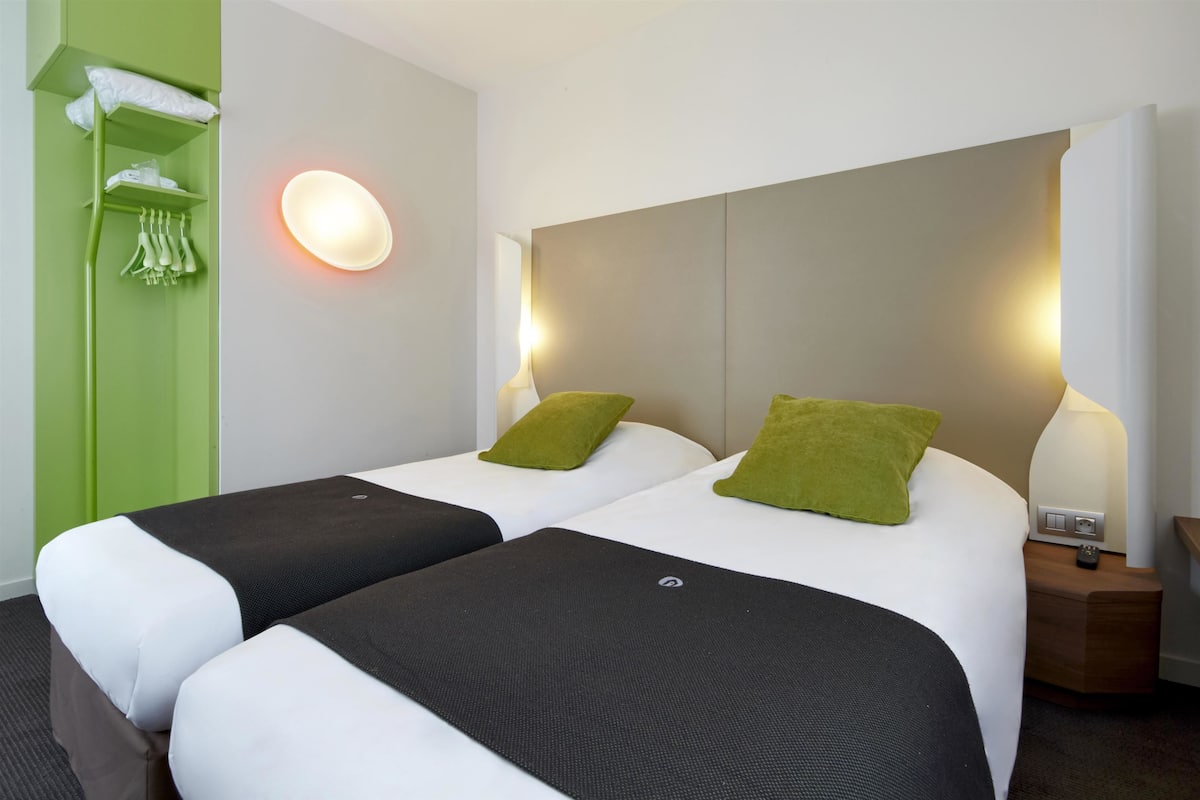 A hotel room with two beds, a green wall, and a nightstand with a lamp.