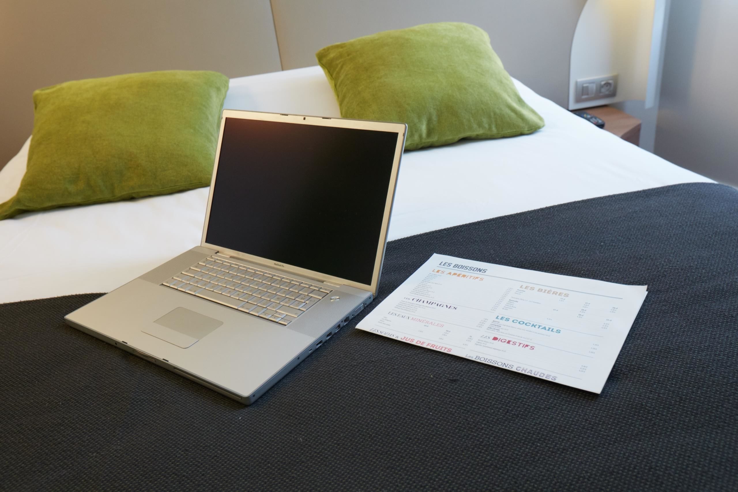 Een laptop op een bed, met een menukaart ernaast.