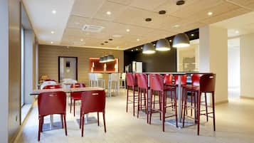 A modern dining area with red chairs and tables, a bar counter, and pendant lighting.