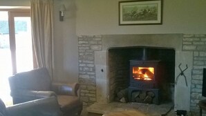A cozy living room with a stone fireplace, leather armchair, and a wooden coffee table. - Battens Farm Cottages - B&B and Self-catering Accommodation (Chippenham)