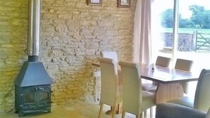 A room with a stone wall, a wooden table with chairs, and a large window with a view of the outdoors. - Battens Farm Cottages - B&B and Self-catering Accommodation (Chippenham)