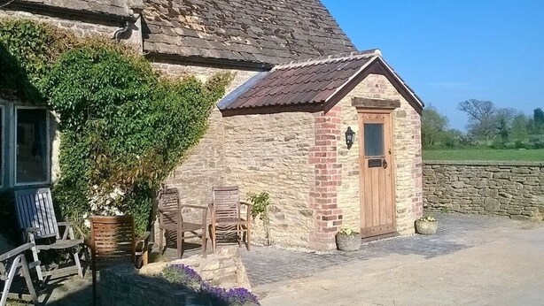 A stone building with a wooden door and a small porch with chairs. - Battens Farm Cottages - B&B and Self-catering Accommodation (Chippenham)