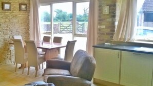 A room with a dining table, chairs, a sofa, and a kitchen area with cabinets. - Battens Farm Cottages - B&B and Self-catering Accommodation (Chippenham)