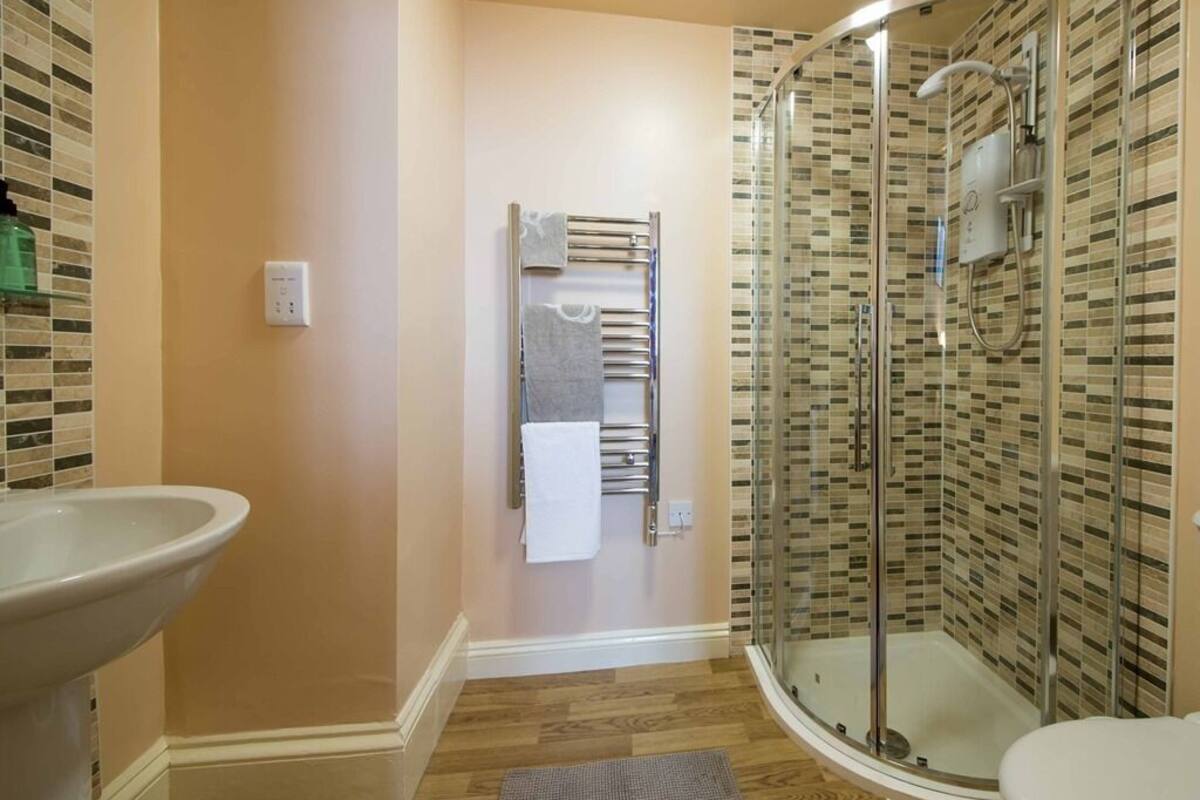 Un baño con cabina de ducha de vidrio, un lavamanos y un perchero para toallas.