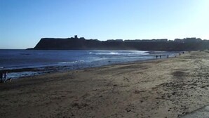 A beach with a sandy shore and a distant view of a fort-like structure. - The Albert (Scarborough)