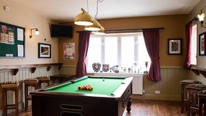A pool table in a room with wooden flooring, a green felt table, and a hanging light fixture. - The Albert (Scarborough)