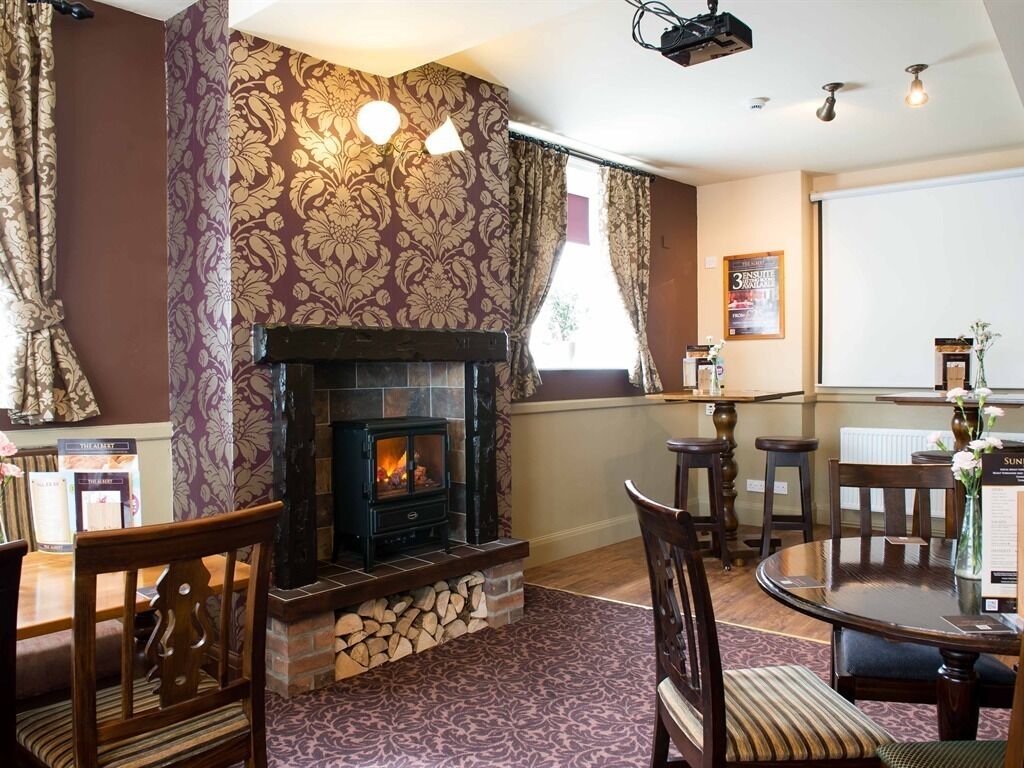 A cozy room with a fireplace, patterned wallpaper, a dining table, and chairs.