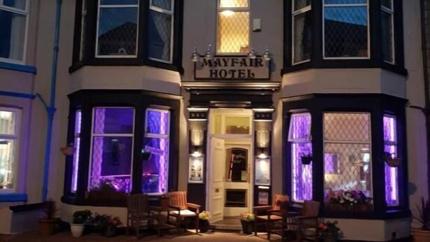 El exterior del Hotel Mayfair, con ventanales iluminados y una fachada tradicional.