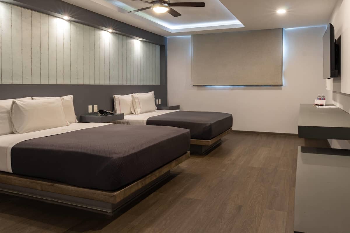 Una habitación de hotel moderna con dos camas, un escritorio, un ventilador de techo y un televisor montado.