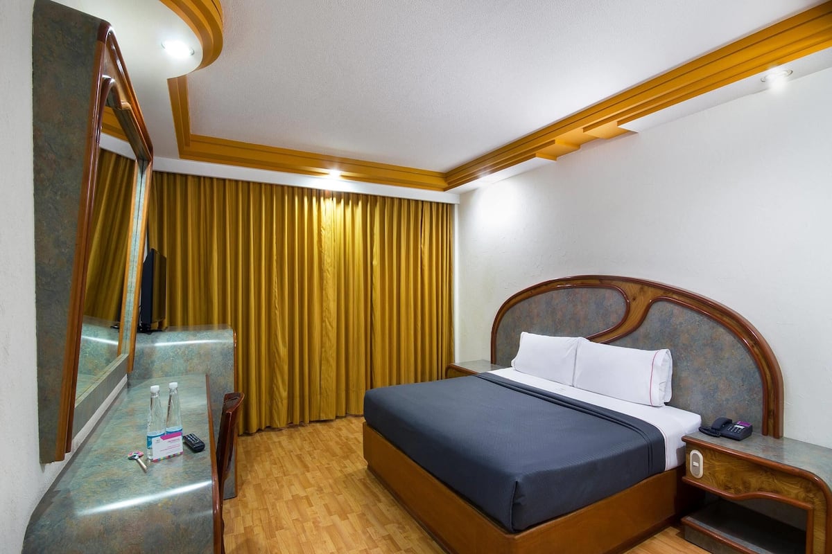 Una habitación de hotel con una cama de madera, una mesita de noche con un teléfono, un espejo y una cortina.