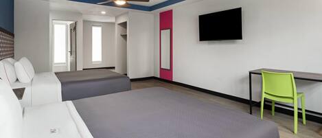 A hotel room with two beds, a desk, a chair, a TV, and a ceiling fan.
