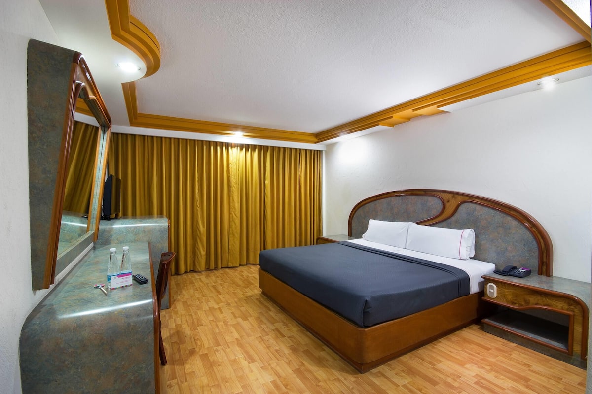 Una habitación de hotel con una cama de madera, una mesita de noche, un espejo y suelo de madera.