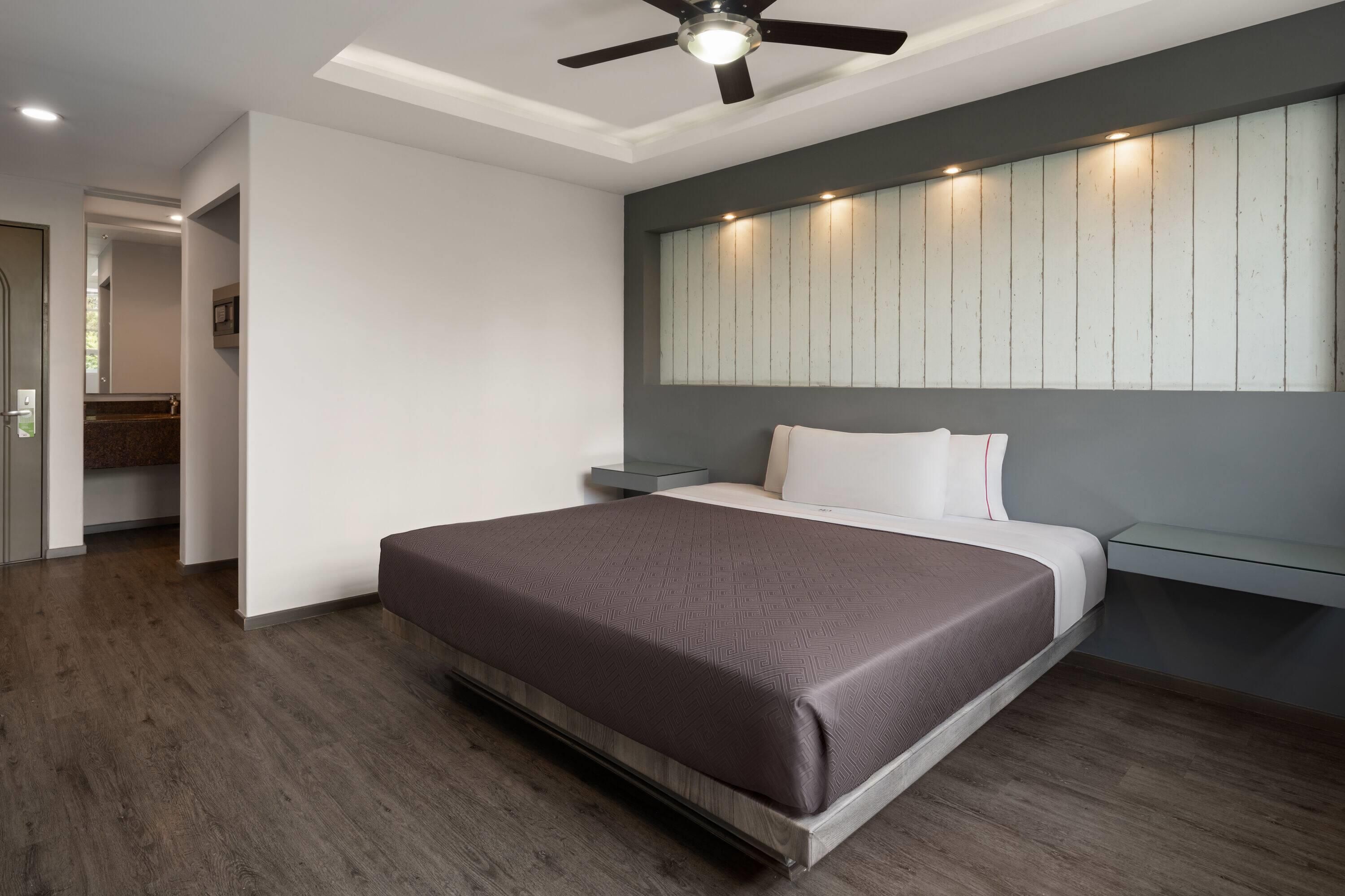 A modern bedroom with a bed, a ceiling fan, a nightstand, and a wall-mounted mirror.