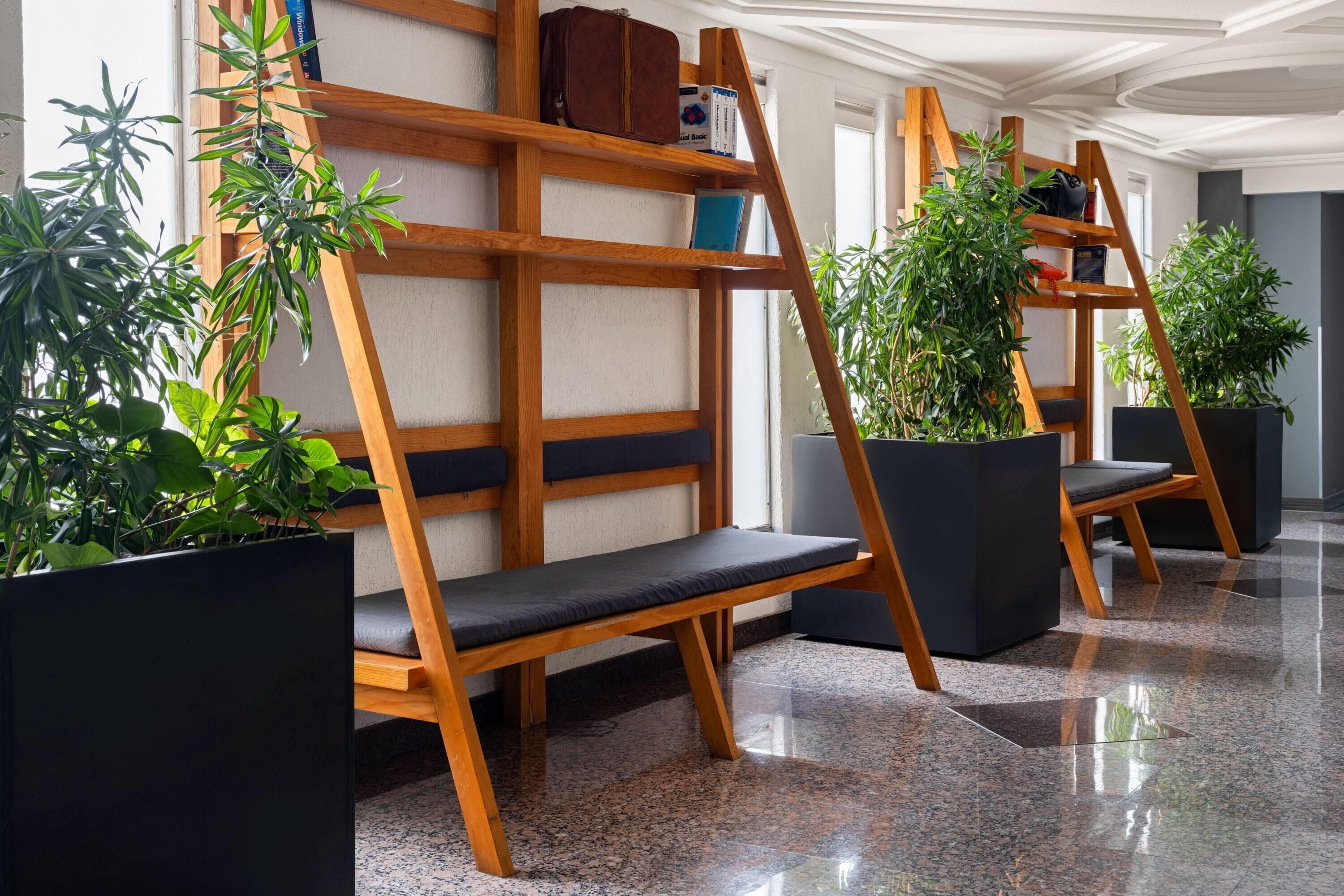 Un moderno vestíbulo de hotel con bancos de madera, plantas en macetas y un suelo de mármol pulido.