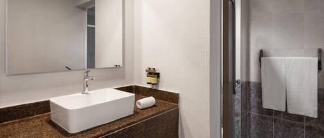 Un baño con lavamanos blanco, un espejo, una toalla y una zona de ducha.