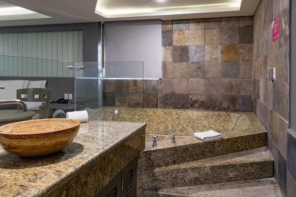 Un baño moderno con encimera de granito, un lavabo grande, cabina de ducha de cristal y pared de piedra.