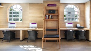 Un espacio de trabajo con dos escritorios, computadoras y sillas. Hay una estantería con libros y un cartel que indica un centro de negocios.