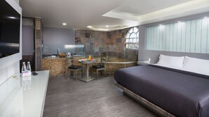 Una habitación de hotel con una cama, un escritorio con televisor, un pequeño comedor con sillas y una pared de piedra.