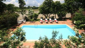 Una piscina rectangular con superficie de agua azul cristalina, rodeada de abundante follaje y árboles.