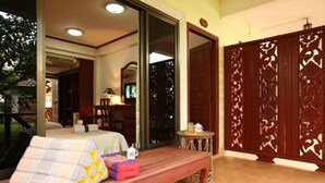 Una habitación con cama, un banco acolchado, una mesita con tetera y un biombo decorativo.