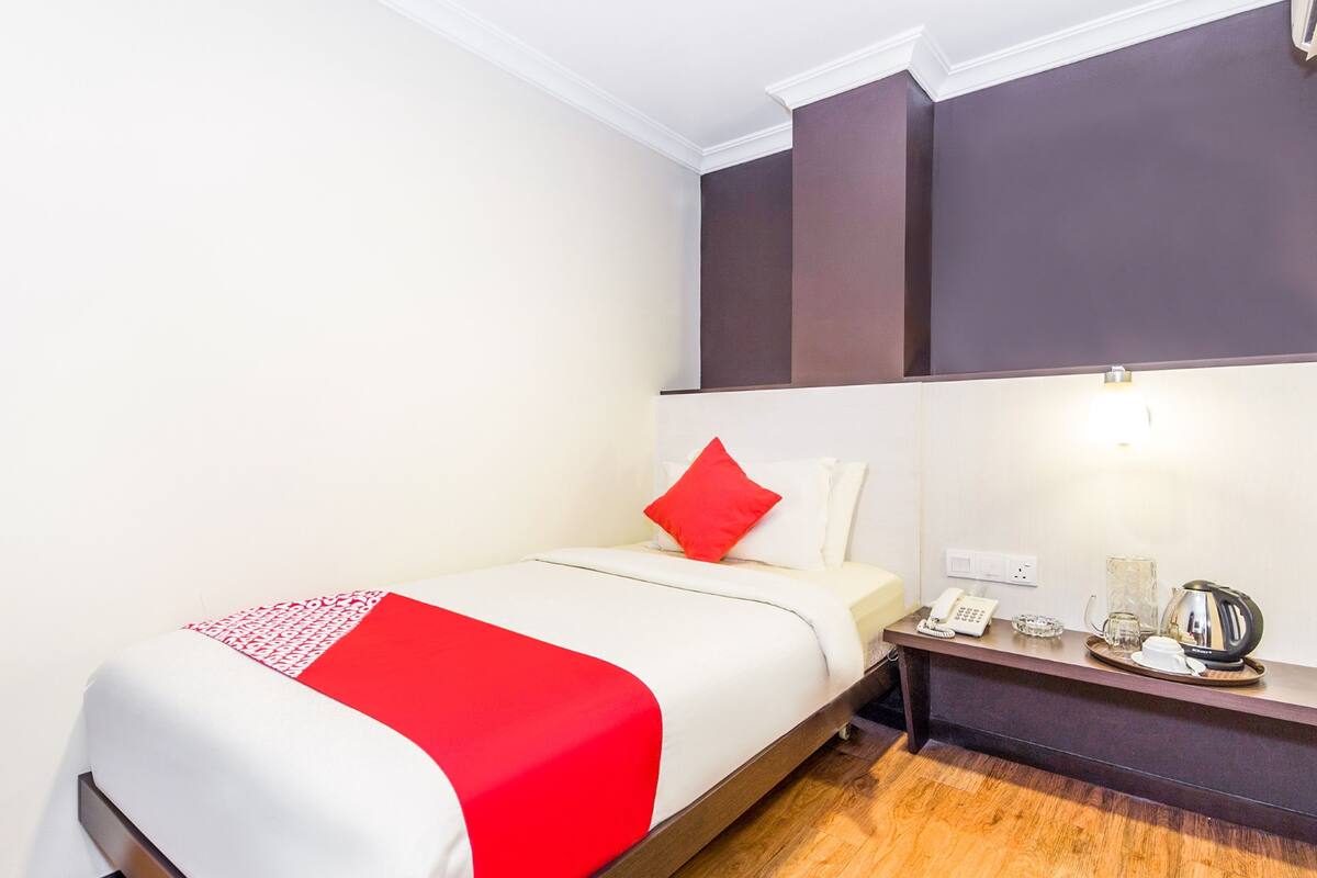 A hotel room with a bed, a bedside table with a phone, a kettle, and a glass.
