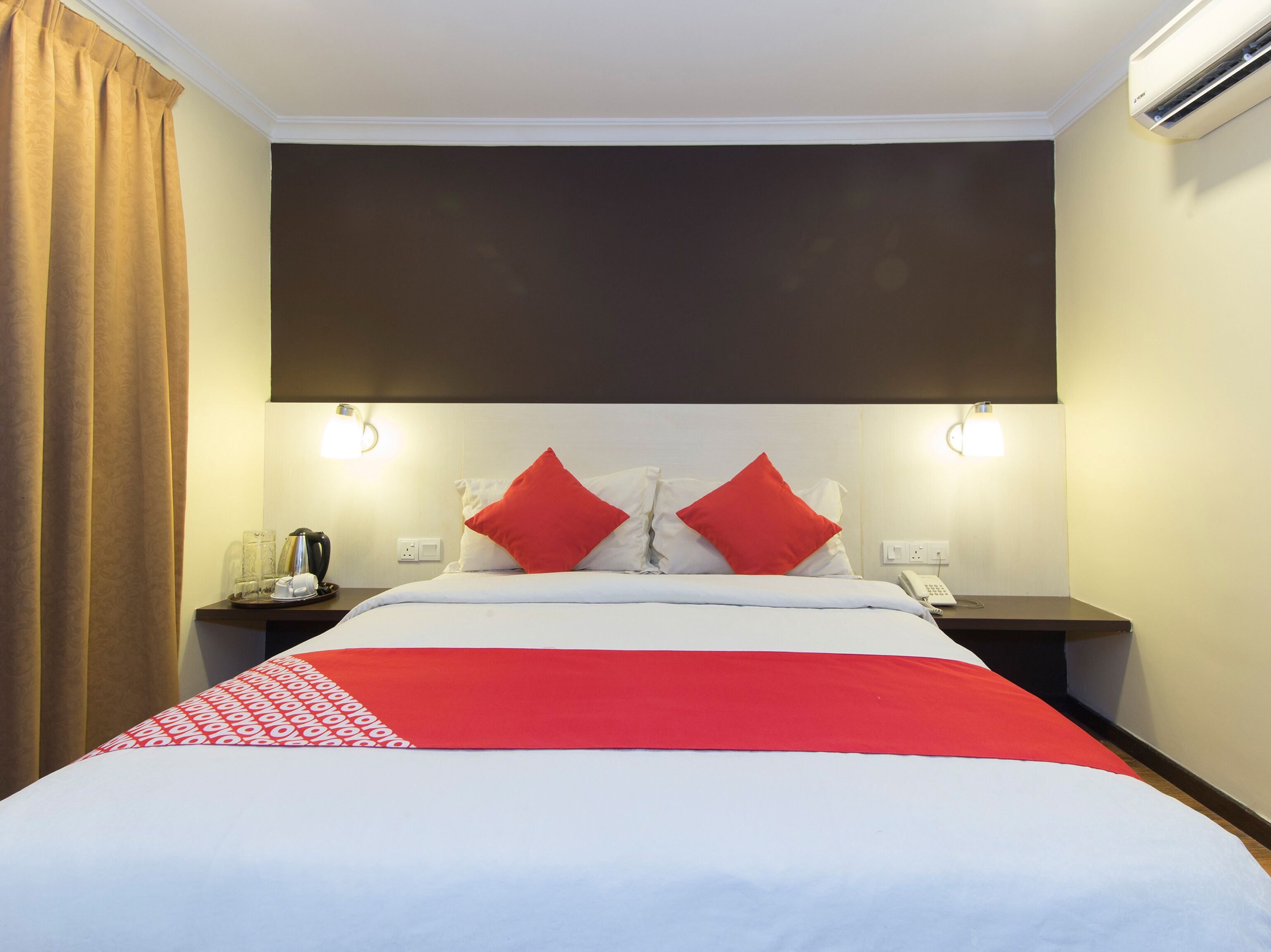 A hotel room with a bed, two bedside tables, a telephone, and an air conditioning unit.