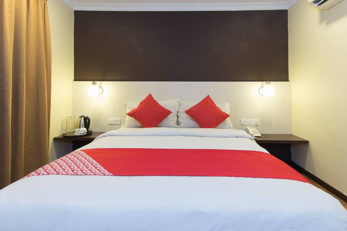 A hotel room with a bed, two bedside tables, a telephone, and an air conditioning unit.
