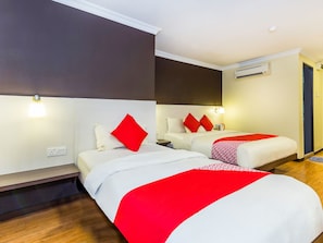 A hotel room with two beds, each with white bedding and red pillows. There is a wooden bench, a bedside table, and a wall-mounted air conditioning unit. - OYO 431 Hotel De Grand Orchard (Kuala Lumpur)