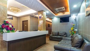 A reception area with a reception desk, a sofa, a floral arrangement, and a wall-mounted TV. - OYO 431 Hotel De Grand Orchard (Kuala Lumpur)