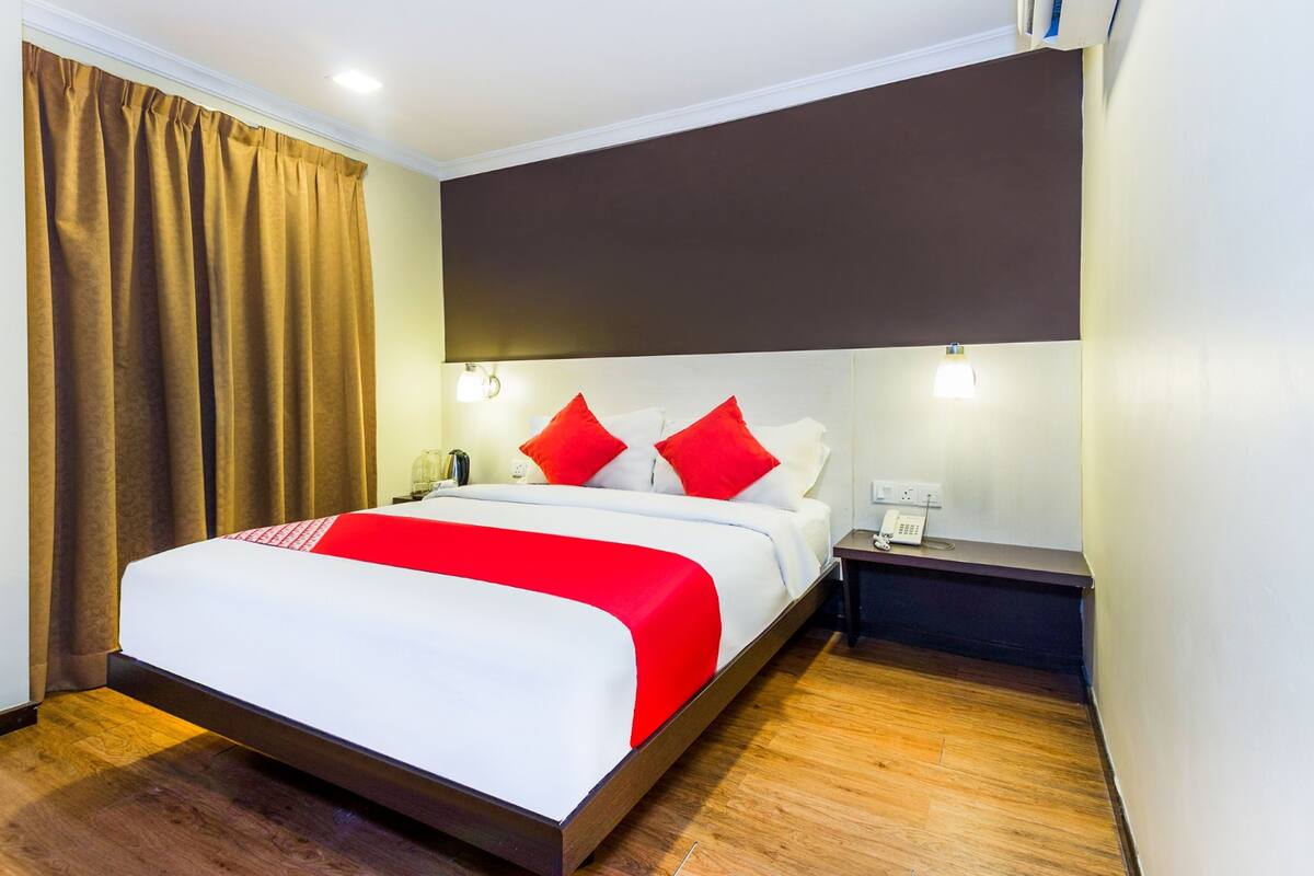 A hotel room with a large bed, red and white bedding, a nightstand with a phone, and a brown headboard.
