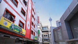 A hotel with a prominent red and white facade, multiple windows, and a view of a tower in the background. - OYO 431 Hotel De Grand Orchard (Kuala Lumpur)