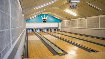 A bowling alley with multiple lanes, a blue wall with a bowling pin design, and overhead lighting.