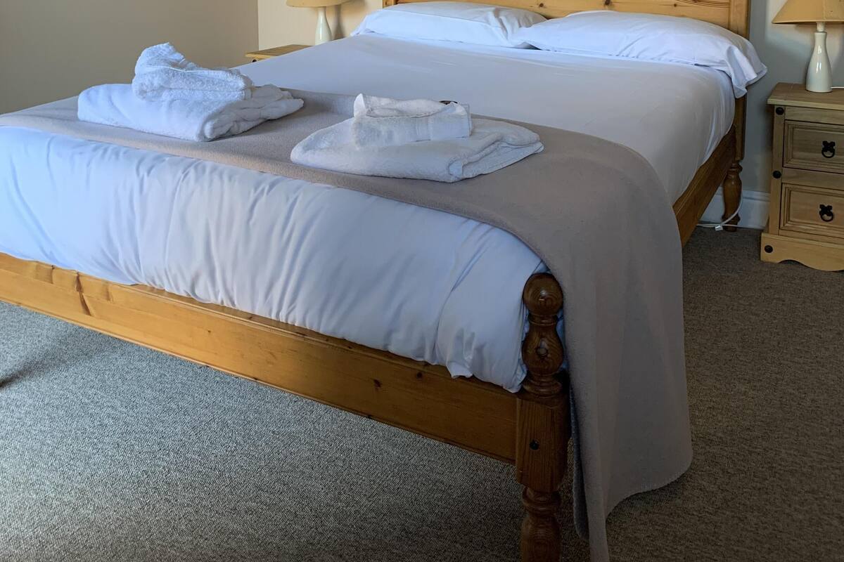 Un lit bien fait, avec du linge de lit et des serviettes blanches, deux lampes de chevet et une table de chevet en bois dotée de tiroirs.