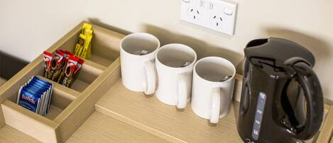 Una encimera de cocina con tres tazas blancas, una tetera eléctrica negra y un cajón que contiene una caja de té Bushells.
