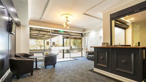 A reception area with a dark wooden reception desk, a large mirror, and a seating area with two chairs and a small table. - Nightcap at Blue Cattle Dog Hotel (St Clair)
