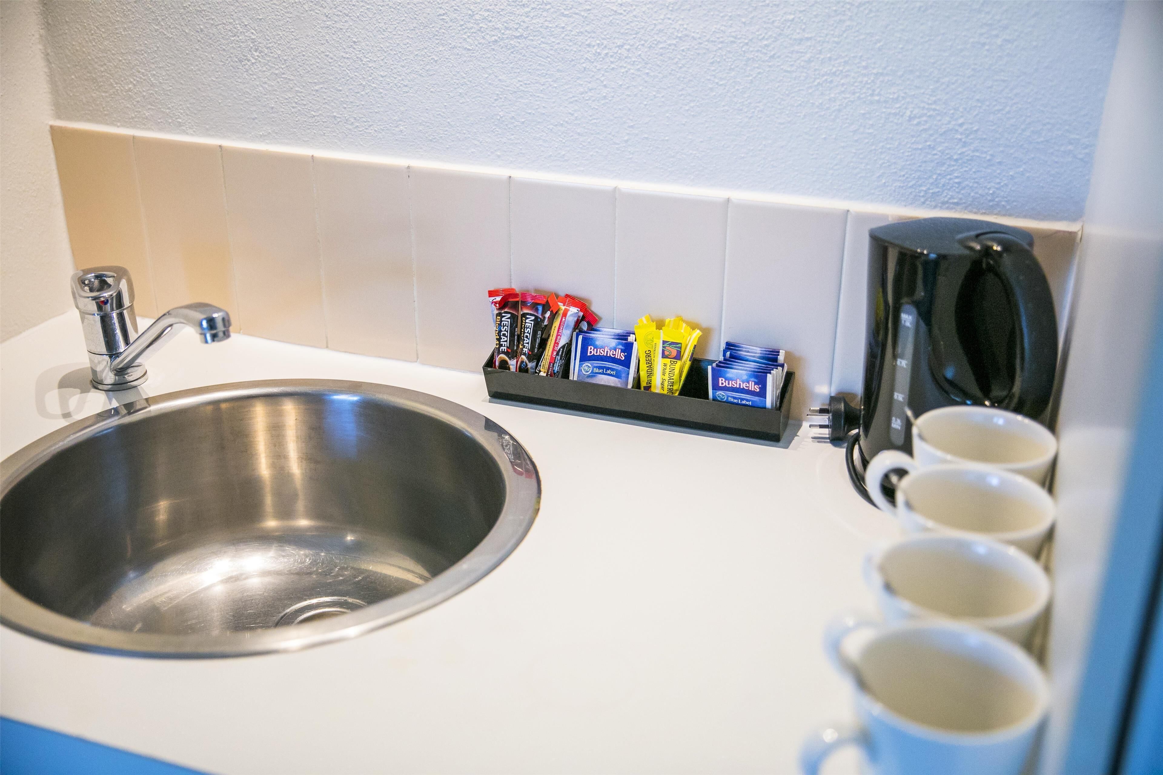A kitchen sink with a faucet, a coffee maker, and a shelf with coffee pods.