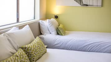 A hotel room with two beds, a window, and a wall-mounted light.