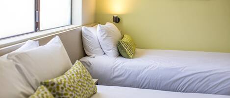 A hotel room with two beds, a window, and a wall-mounted light.