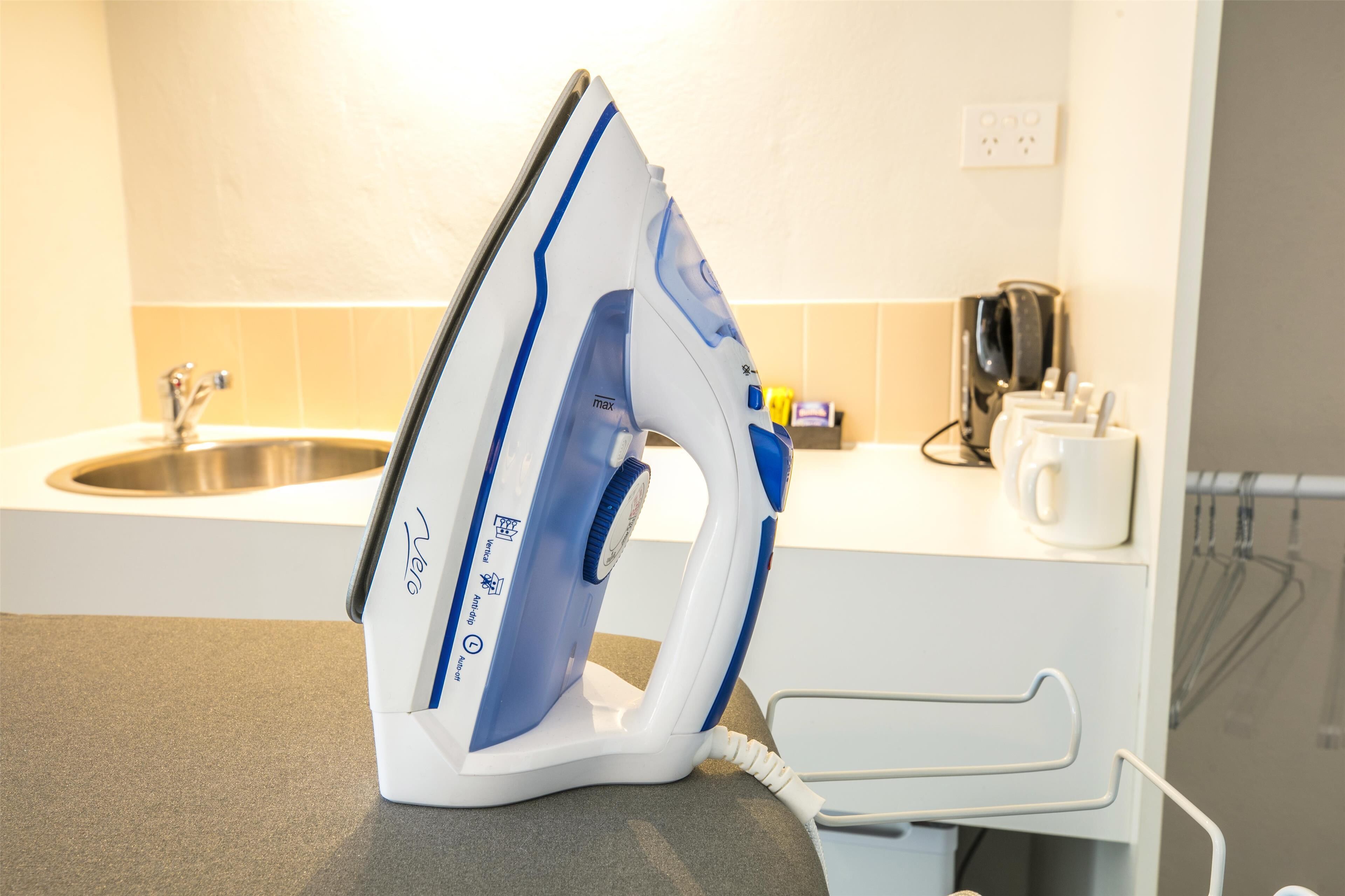A white and blue iron on a kitchen counter with a sink and a kettle in the background.