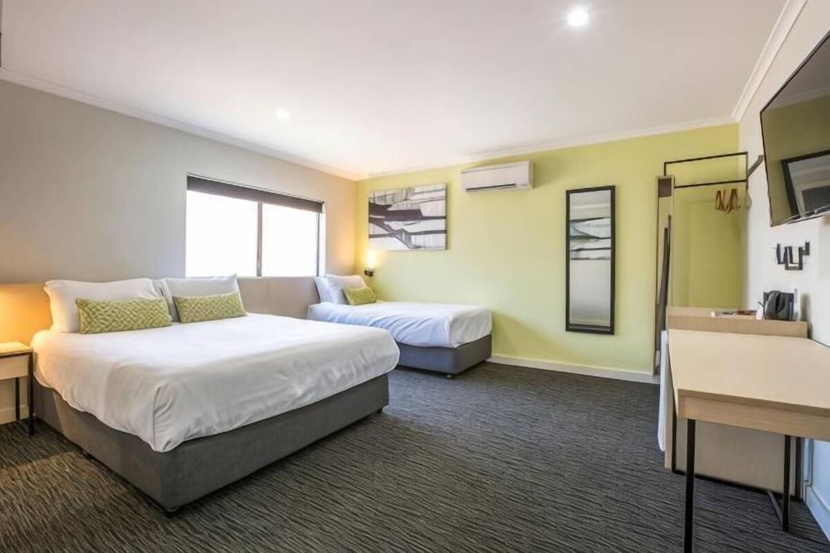 A hotel room with a large bed, a smaller bed, a desk, and a mirror.