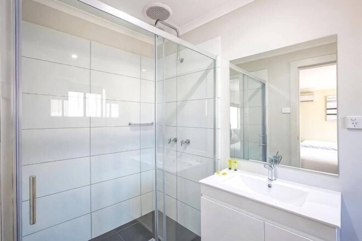 A modern bathroom with a glass-enclosed shower, a white sink, and a large mirror.
