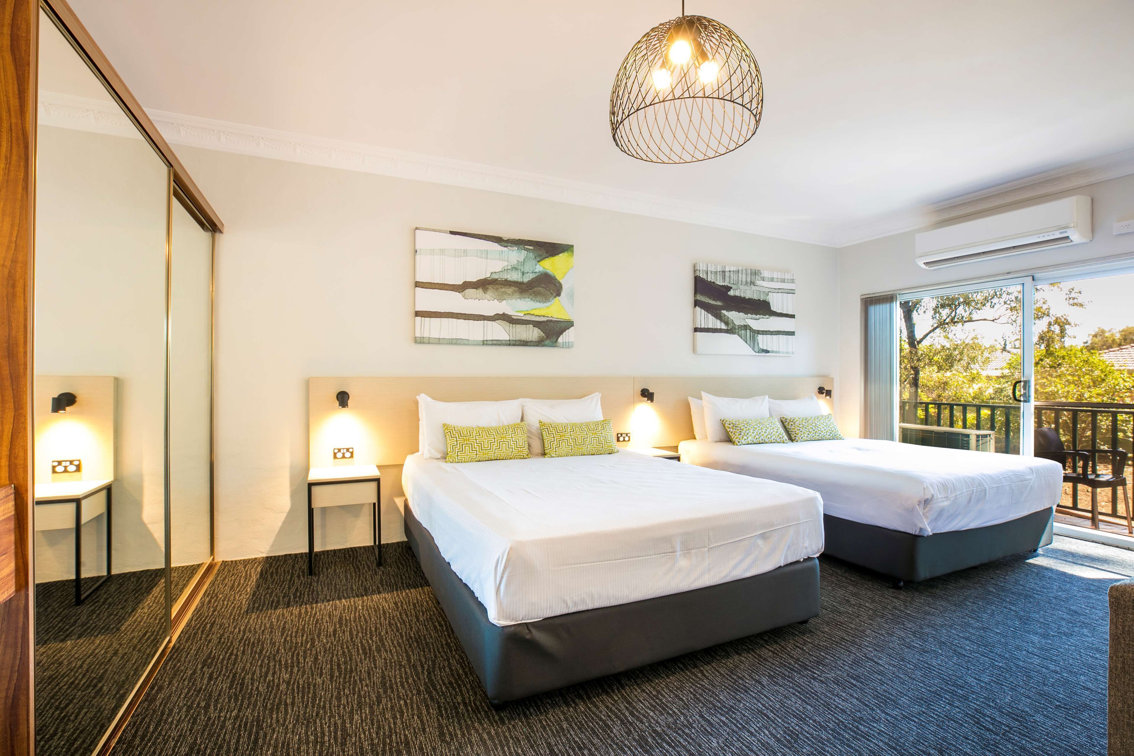 A hotel room with two beds, a large mirror, artwork on the walls, and a balcony with a view.