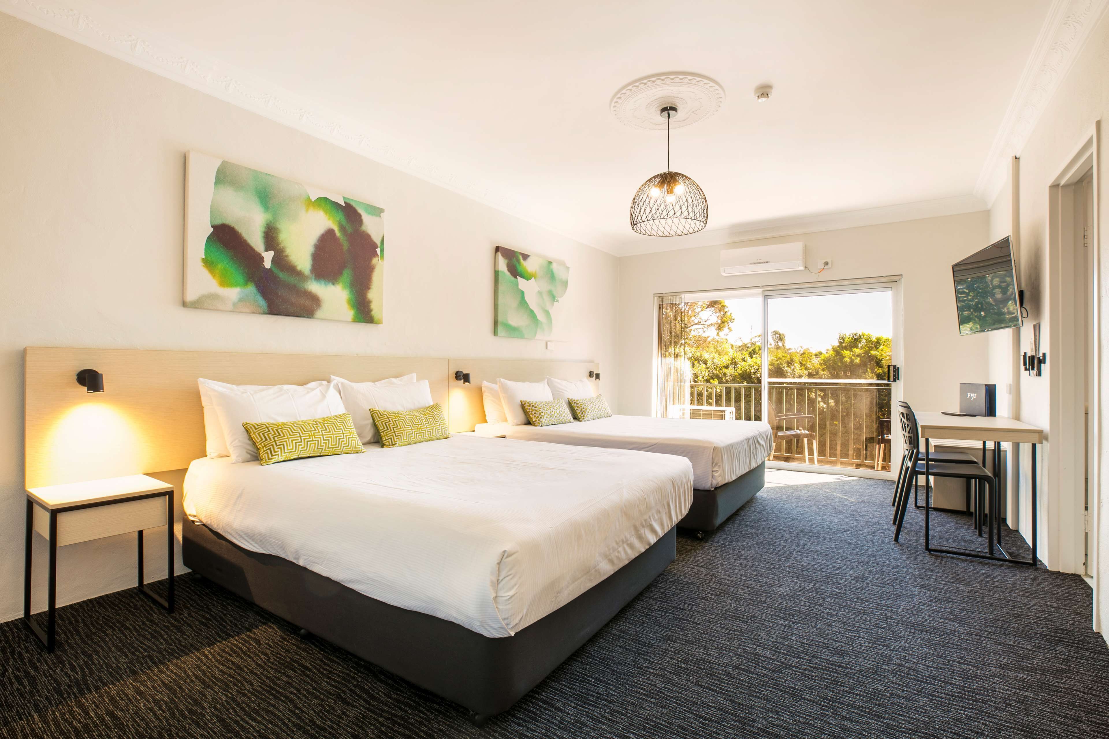 Habitación de hotel con dos camas, un escritorio y un balcón con vistas.