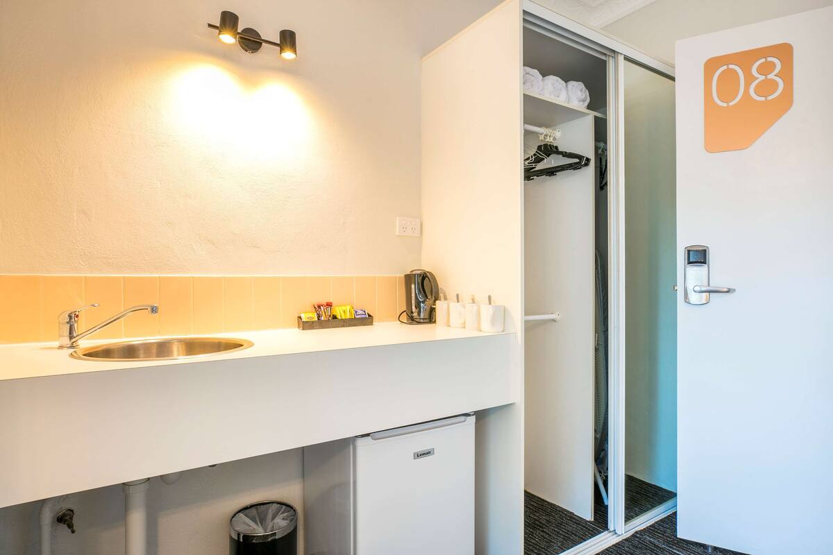 A hotel room with a white sink, a mirror, a small refrigerator, a shower area, and a door marked with the number 08.